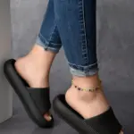 Pantuflas negras de suela EVA con textura acanalada y diseño tipo slide, vistas de perfil para resaltar su grosor y comodidad.