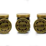 Tres pilas de tarros de grasa para cuero LION en color dorado y negro, acompañados de tapas circulares con diseño ornamentado.