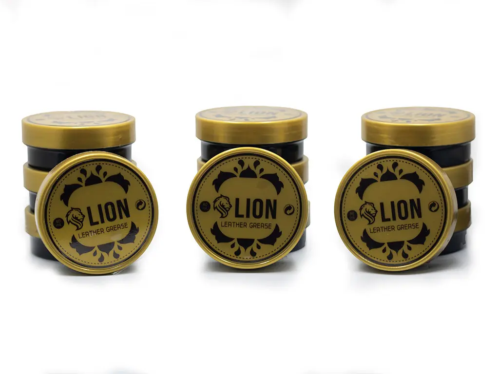 Tres pilas de tarros de grasa para cuero LION en color dorado y negro, acompañados de tapas circulares con diseño ornamentado.