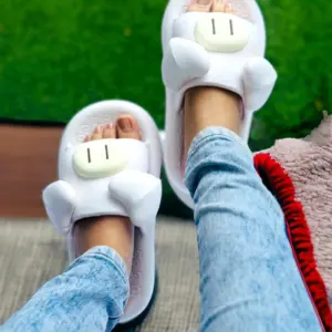 Pantuflas de descanso blancas para mujer con diseño de cerdito, suela acolchada, orejas 3D y hocico en relieve, usadas con jeans sobre césped.