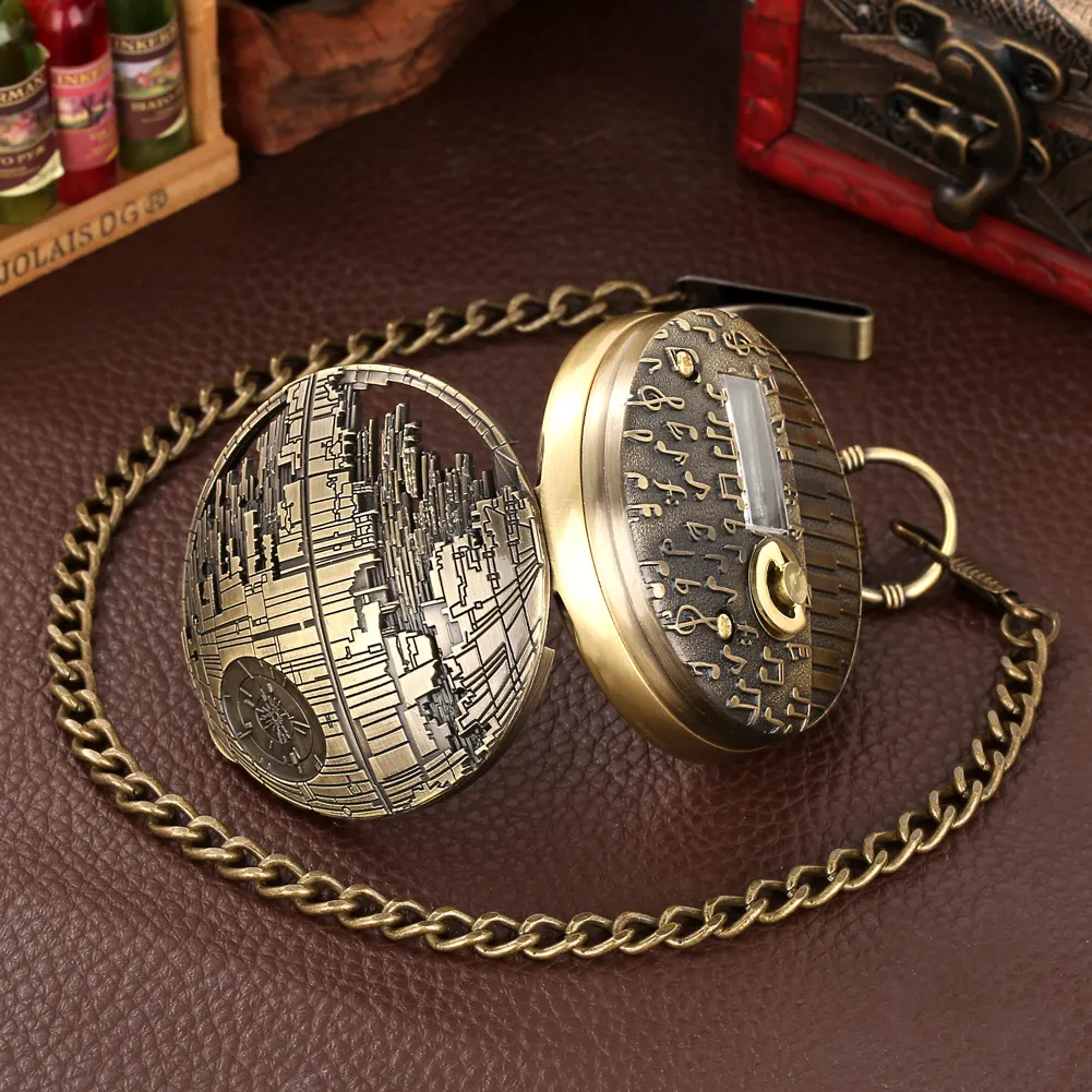 Reloj de bolsillo vintage dorado con diseño de la Estrella de la Muerte y caja de música, abierto sobre superficie de cuero marrón con cadena metálica.
