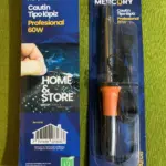 Cautín tipo lápiz Mercury de 60W con mango naranja y punta fina, en empaque de blíster con cable, junto a su cartón sobre fondo verde.