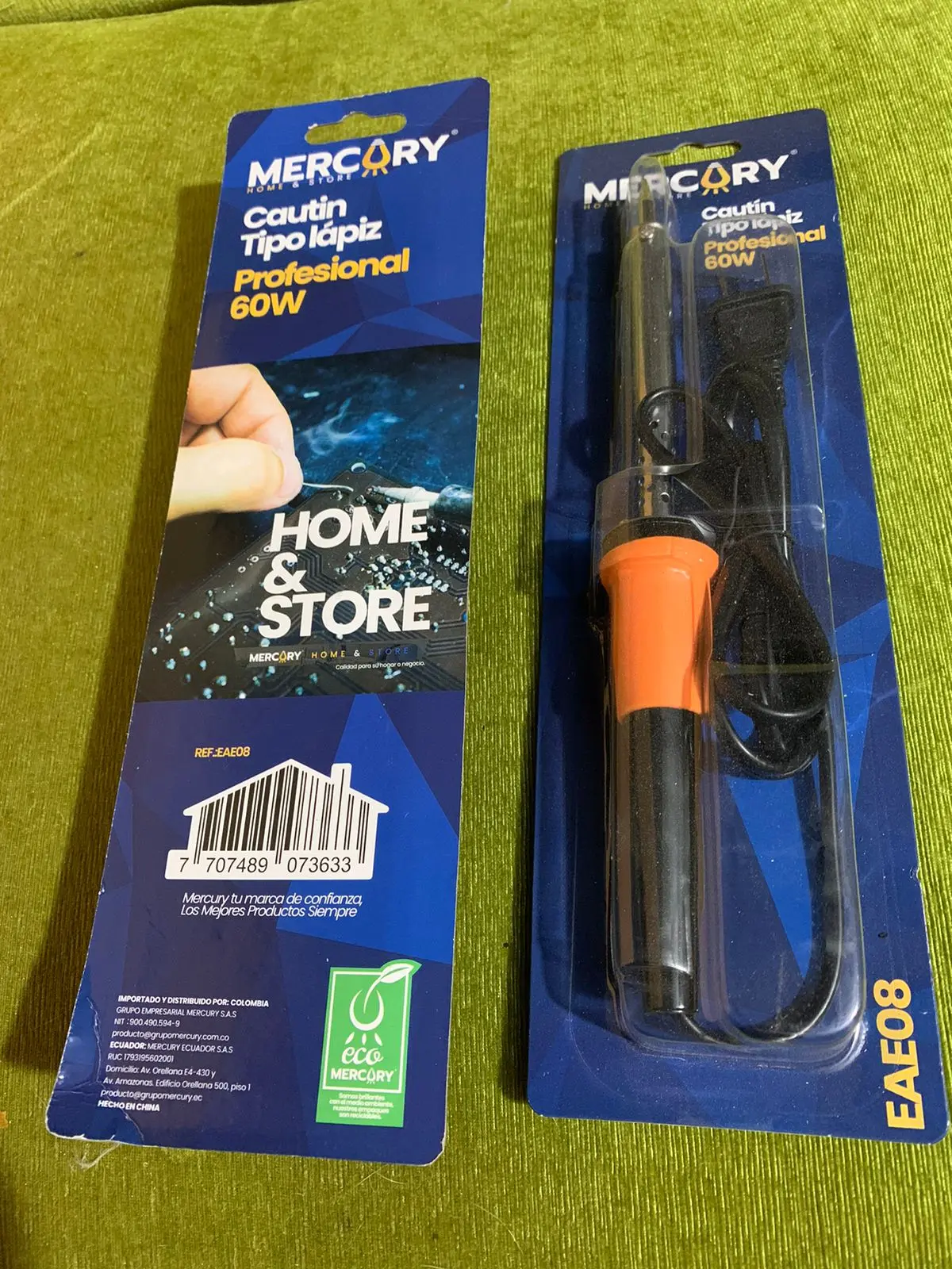 Blíster con cautín tipo lápiz Mercury 60W de mango naranja y cable negro junto al empaque de cartón azul sobre fondo verde.