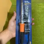 Cautín tipo lápiz Mercury de 60W con mango naranja y negro, punta fina y cable con enchufe, empacado en blíster azul y sostenido por una mano.