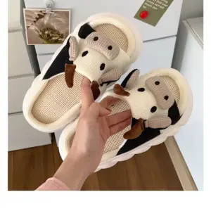 Pantuflas de peluche con diseño de vaca en blanco y negro, cara en relieve y suela blanca gruesa, ideales para descanso en casa.