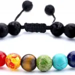 Pulsera artesanal de roca volcánica negra texturizada con siete cuentas de colores para chakras y cierre ajustable.