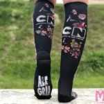 Medias de compresión negras Cartoon Network para piernas cansadas, diseño estampado con personajes animados y suela con texto gris.