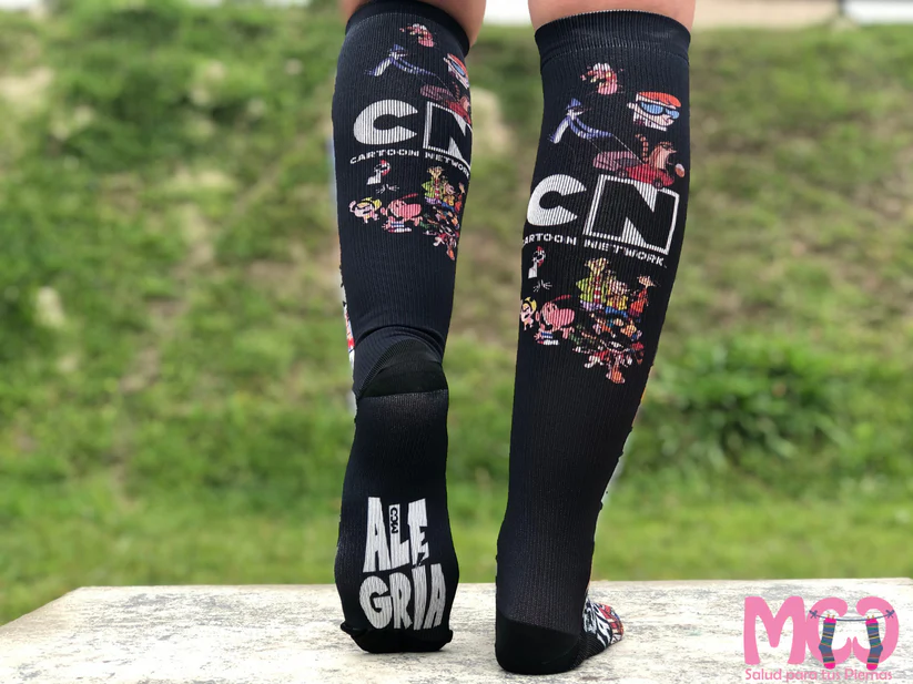 Medias de compresión negras Cartoon Network para piernas cansadas, diseño estampado con personajes animados y suela con texto gris.