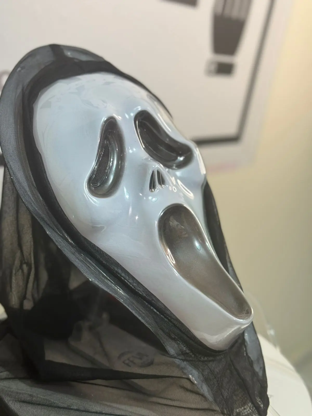 Máscara blanca de expresión de grito con capucha de tela negra tipo malla, vista lateral en primer plano para disfraz de Halloween.