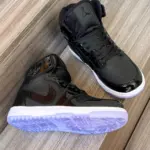 Tenis deportivos Jordan de caña alta en charol negro brillante con suela translúcida violeta, vistos desde ángulo superior y lateral sobre superficie de madera.