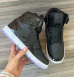 Tenis Jordan negros de caña alta en charol brillante con suela morada translúcida, sostenidos en mano sobre superficie de madera.