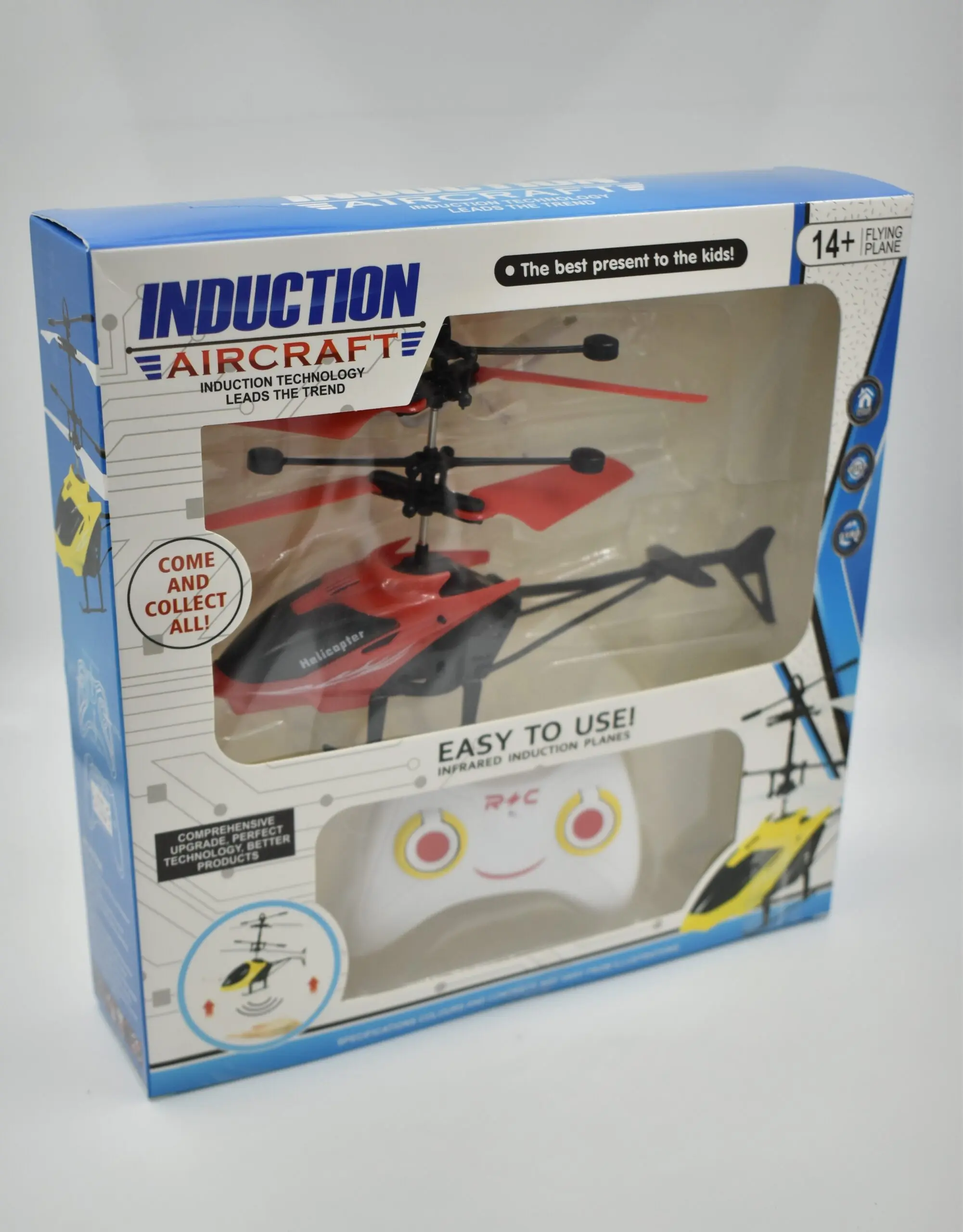 Empaque de helicóptero rojo y negro con hélices rojas y control remoto blanco con diseño de cara sonriente, listo para vuelo en interiores.
