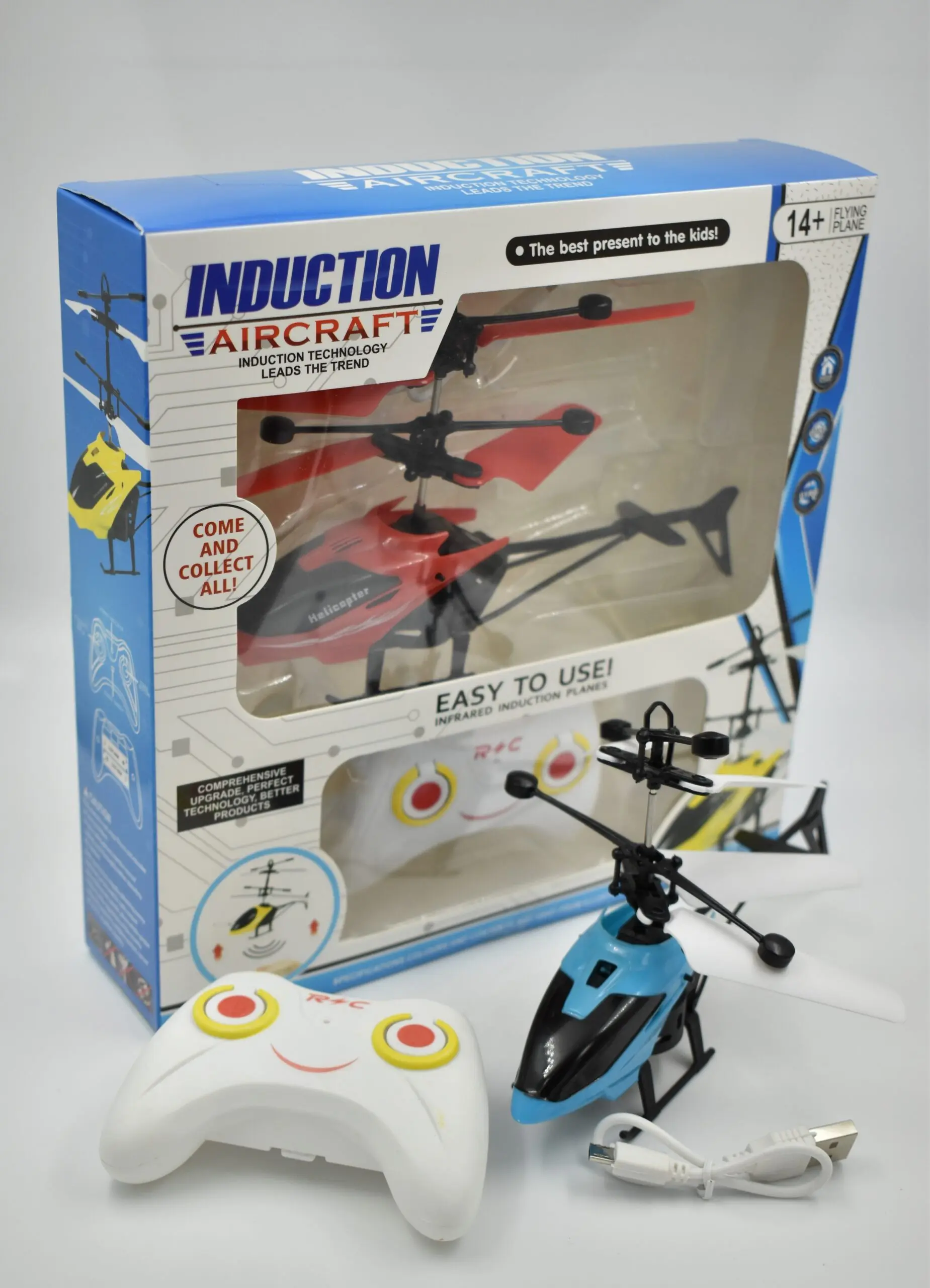 Helicóptero azul y negro, control remoto blanco con diseño de cara sonriente, cable USB y caja de empaque con modelo rojo.