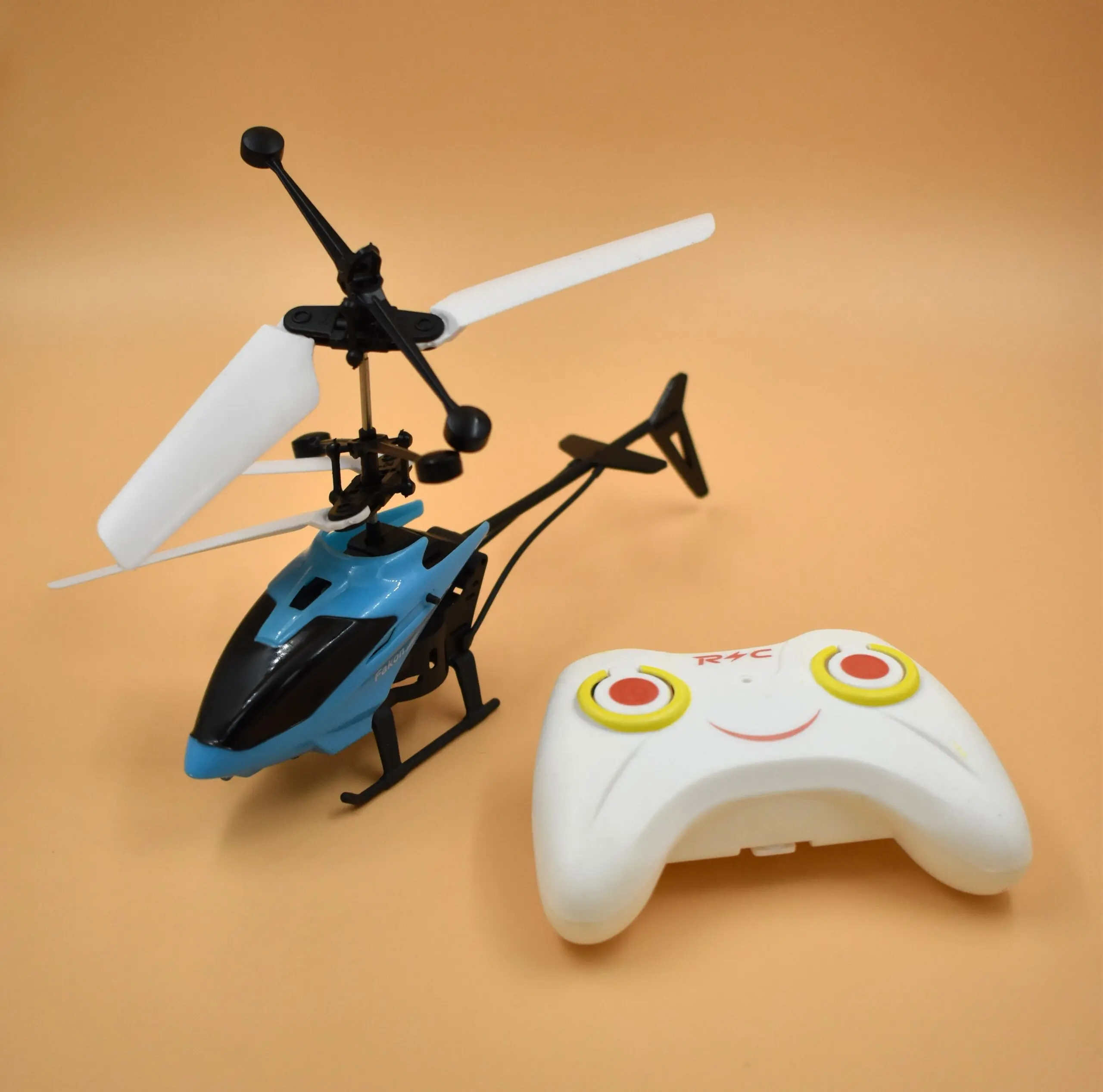 Helicóptero azul y negro con hélices blancas y control remoto blanco con botones amarillos y rojos sobre fondo beige.