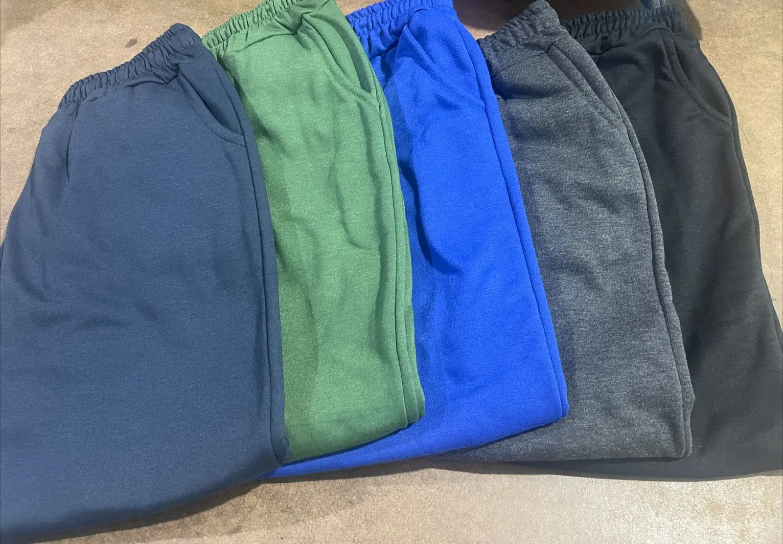 Cinco pantalones deportivos de algodón en colores azul, verde, azul rey, gris y negro con cintura elástica y bolsillos laterales.