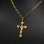 Collar de acero inoxidable dorado con cadena texturizada y dije de crucifijo con relieves circulares en los extremos sobre fondo negro.