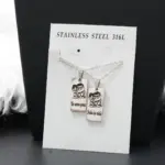 Collar doble para pareja en acero inoxidable plateado con dos dijes rectangulares grabados con personajes y frase romántica.