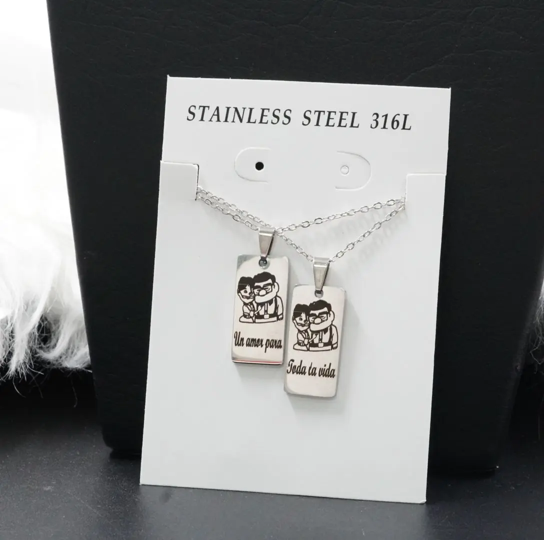 Collar doble para pareja en acero inoxidable plateado con dos dijes rectangulares grabados con personajes y frase romántica.