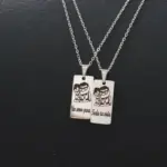 Par de collares en acero inoxidable con dijes rectangulares grabados con personajes y texto romántico sobre fondo negro