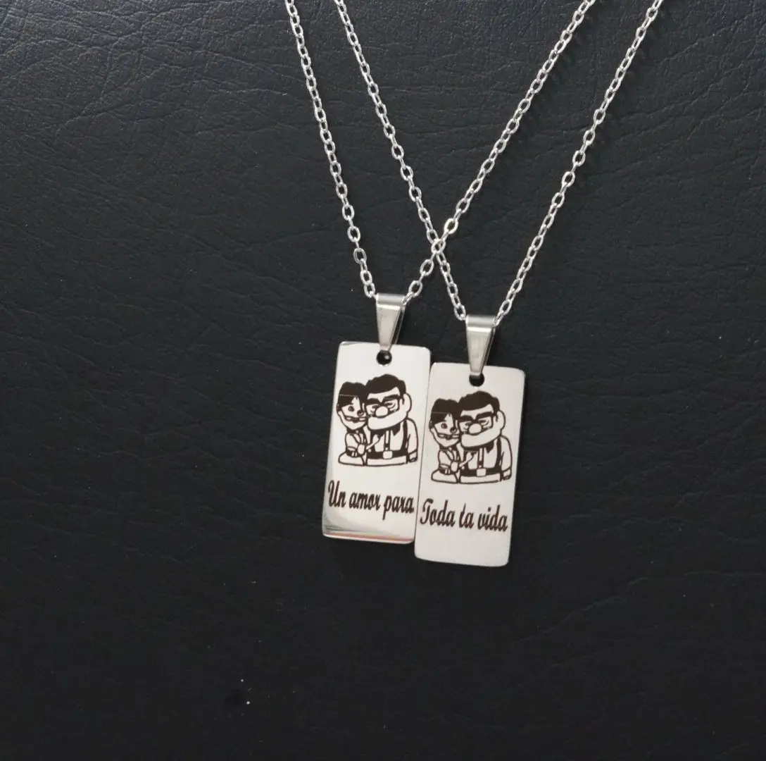 Par de collares en acero inoxidable con dijes rectangulares grabados con personajes y texto romántico sobre fondo negro