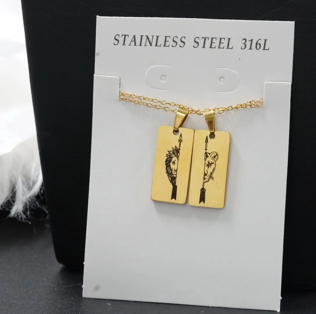 Collar de pareja en acero inoxidable dorado con dos dijes de placa rectangular, grabados con la mitad de un león y una flecha.
