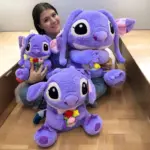 Peluche gigante morado Angel de 90 cm con flores en las manos, sentado en el piso junto a dos versiones más pequeñas.