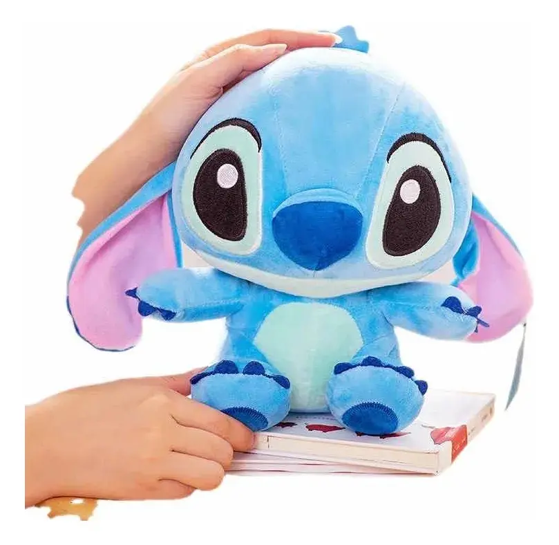 Peluche de Stitch azul con orejas rosadas y vientre celeste, de textura suave, sostenido por manos sobre un libro blanco.