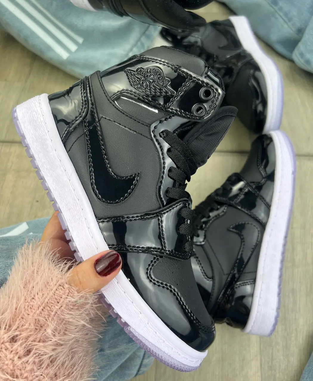 Tenis deportivos Jordan en charol negro de caña alta sostenidos en mano, con suela blanca y detalles brillantes.
