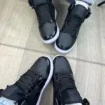 Tenis deportivos Jordan de caña alta en color negro brillante, fotografiados desde arriba mostrando ambas zapatillas con suelas blancas.