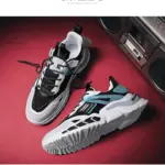 Zapatillas urbanas blancas para hombre con detalles negros y celestes, diseño chunky y suela track, dispuestas sobre superficie roja junto a grabadora.