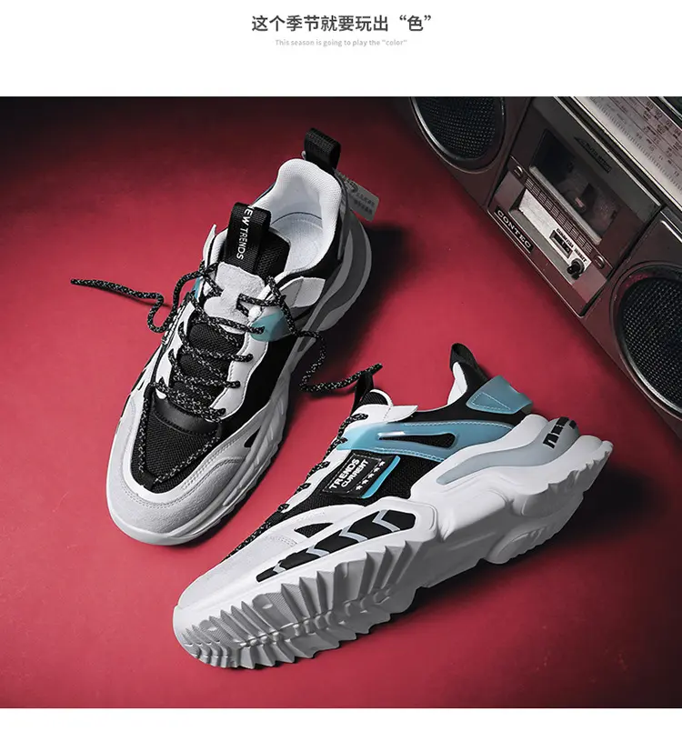Zapatillas urbanas blancas para hombre con detalles negros y celestes, diseño chunky y suela track, dispuestas sobre superficie roja junto a grabadora.