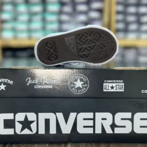 Suela de goma marrón con patrón geométrico antideslizante de un zapato infantil Converse apoyado sobre una caja negra con el logo de la marca en blanco.