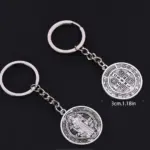 Dos llaveros metálicos plateados con la medalla de San Benito de 3 cm, que muestran ambos lados con detalles grabados y argolla de acero.