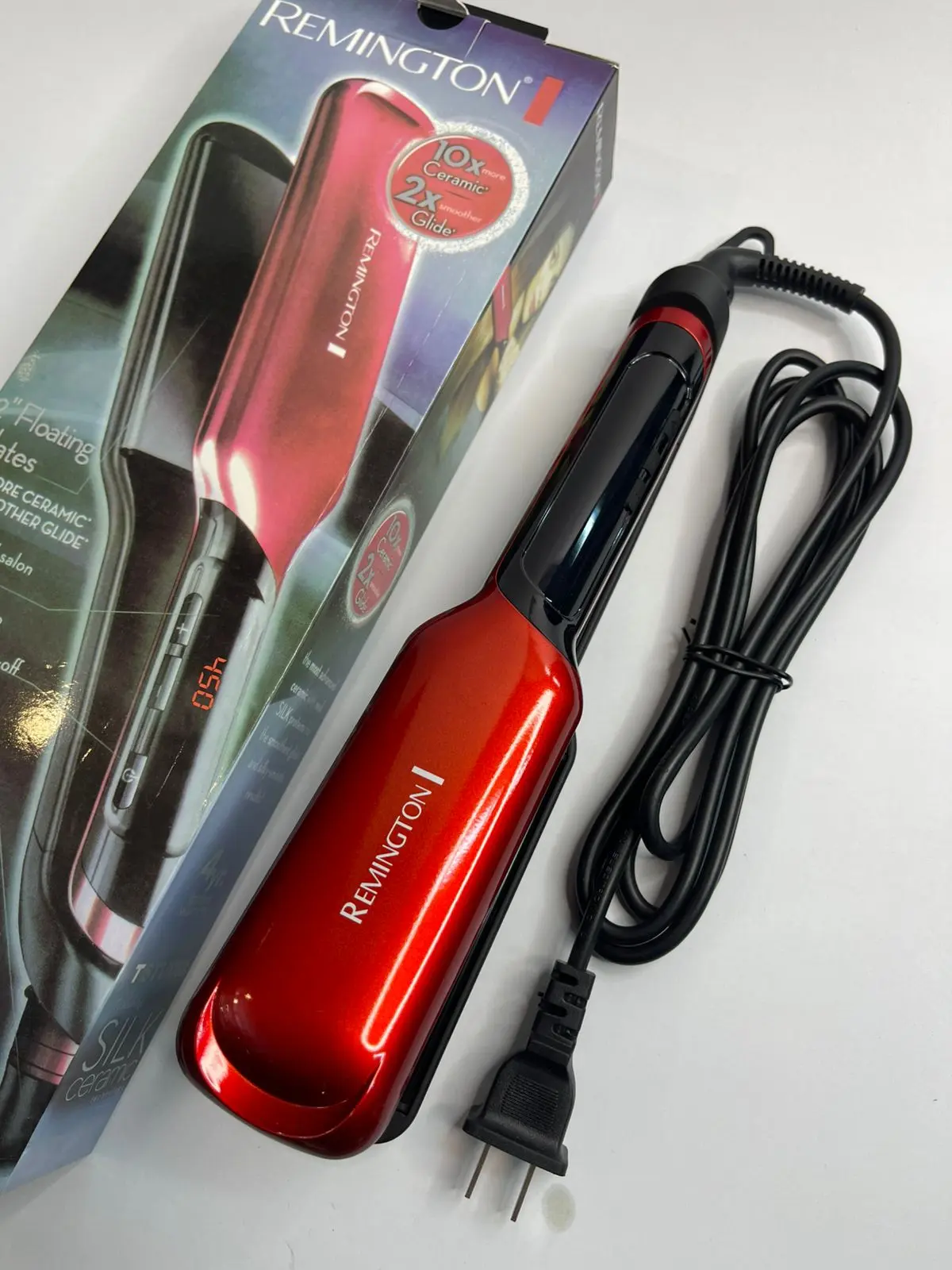 Plancha de cabello Remington Silk de acabado metálico rojo con cable negro, junto a su caja de empaque sobre fondo blanco.