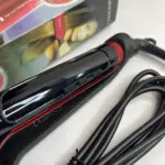 Plancha de cabello Remington roja con placas anchas de microcerámica, cable negro enrollado y caja original al fondo.
