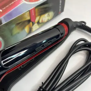 Plancha de cabello Remington roja con placas anchas de microcerámica, cable negro enrollado y caja original al fondo.