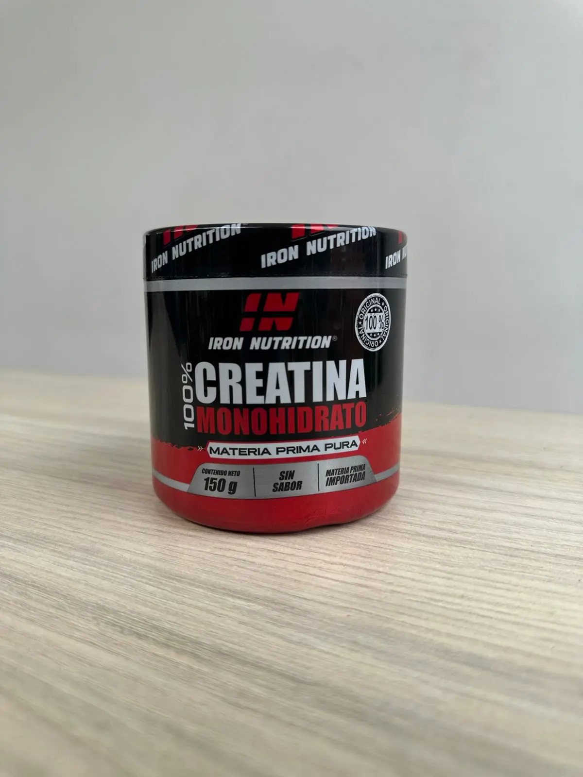 Envase cilíndrico negro con detalles rojos de creatina monohidrato en polvo Iron Nutrition, presentación de 150 gramos sobre una superficie de madera.