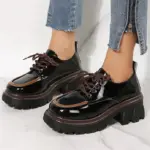 Zapatos Cairluxe de plataforma con suela dentada, diseño en charol negro con borde y cordones color café, lucidos con jeans de cremallera lateral.