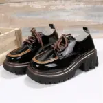 Zapatos Cairluxe de plataforma con suela dentada, acabado en charol negro, detalle de borde color caramelo y cordones marrones sobre superficie blanca.