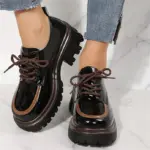 Zapatos Cairluxe de plataforma con suela dentada, diseño en charol negro y detalle de borde café, cordones marrones y acabado brillante.