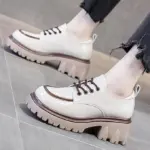 Zapatos de plataforma Cairluxe en charol marfil con suela gruesa track marrón, cordones oscuros y costuras decorativas.