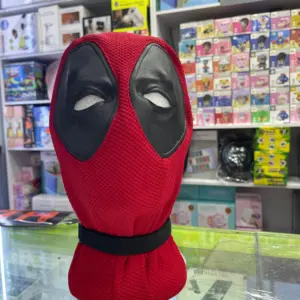 Máscara de Deadpool de tela roja con textura de malla transpirable y parches negros en los ojos, sobre un soporte en una tienda.