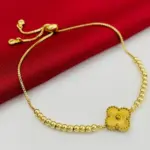 Pulsera dorada ajustable con abalorios redondos y dije central tipo flor estriada, dispuesta sobre tela roja y superficie blanca.