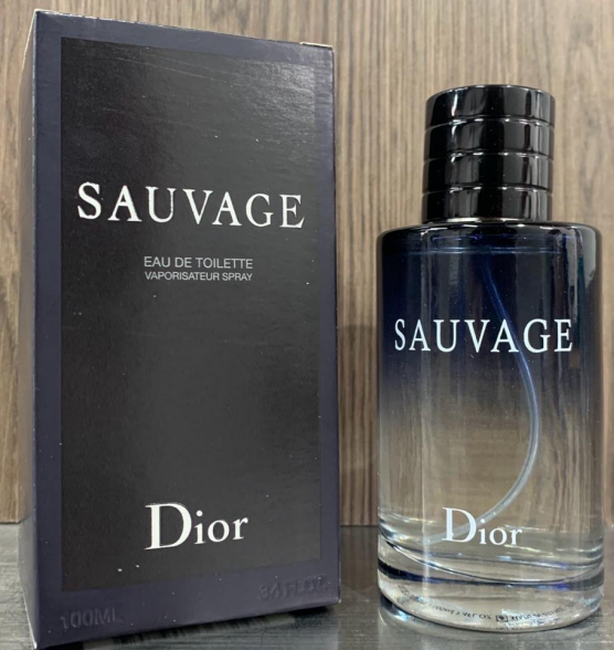 Perfume Dior Sauvage Eau de Toilette de 100 ml con frasco de vidrio degradado azul y tapa negra junto a su caja azul oscuro sobre madera.