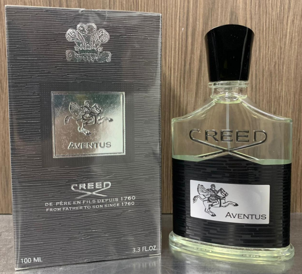 Perfume Creed Aventus de 100 ml con frasco de vidrio texturizado negro, líquido transparente y caja gris plomada con relieve plateado.