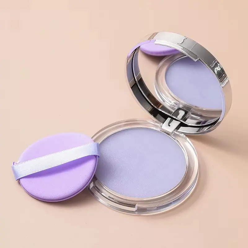 Polvo matificante compacto color lavanda en estuche transparente con espejo y esponja de aplicación morada sobre fondo beige.