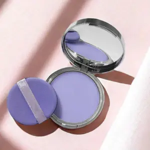 Polvo matificante compacto color lavanda en estuche plateado abierto con espejo y aplicador circular morado sobre fondo rosa.