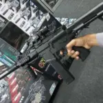 Pistola de hidrogel Arp9 negra con mira holográfica y accesorios tácticos, sostenida por una mano sobre cajas de empaque.