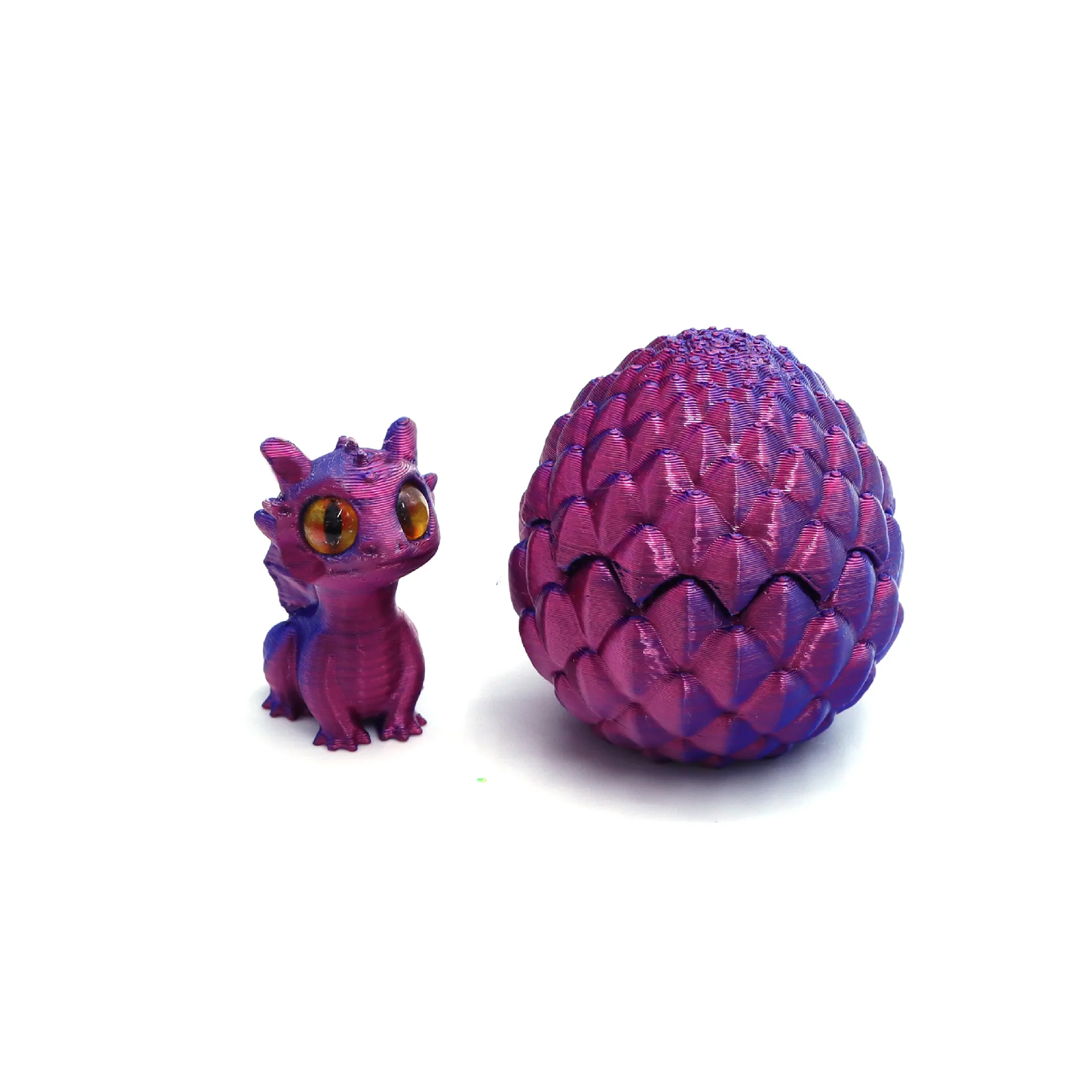 Mini dragón morado con ojos naranjas junto a un huevo con textura de escamas, ambos en color morado.