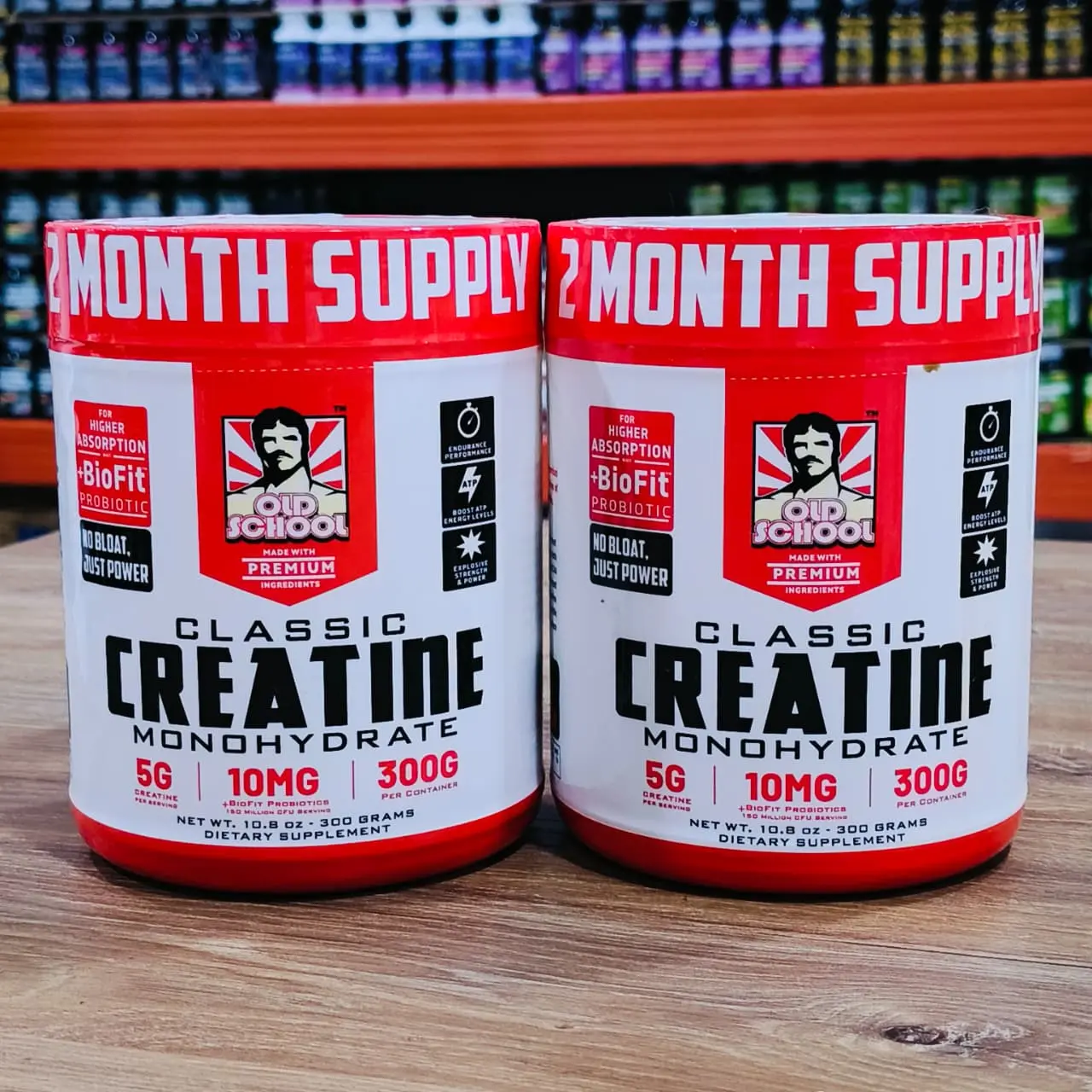 Set de dos tarros de Creatina Monohidrato Old School con BioFit de 300g, color blanco y rojo, sobre superficie de madera en tienda.